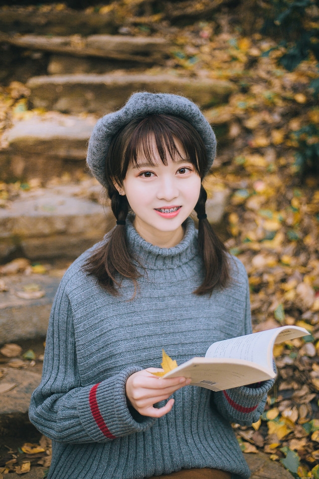 贝雷帽麻花辫美女落叶下安静看书露牙套浅笑