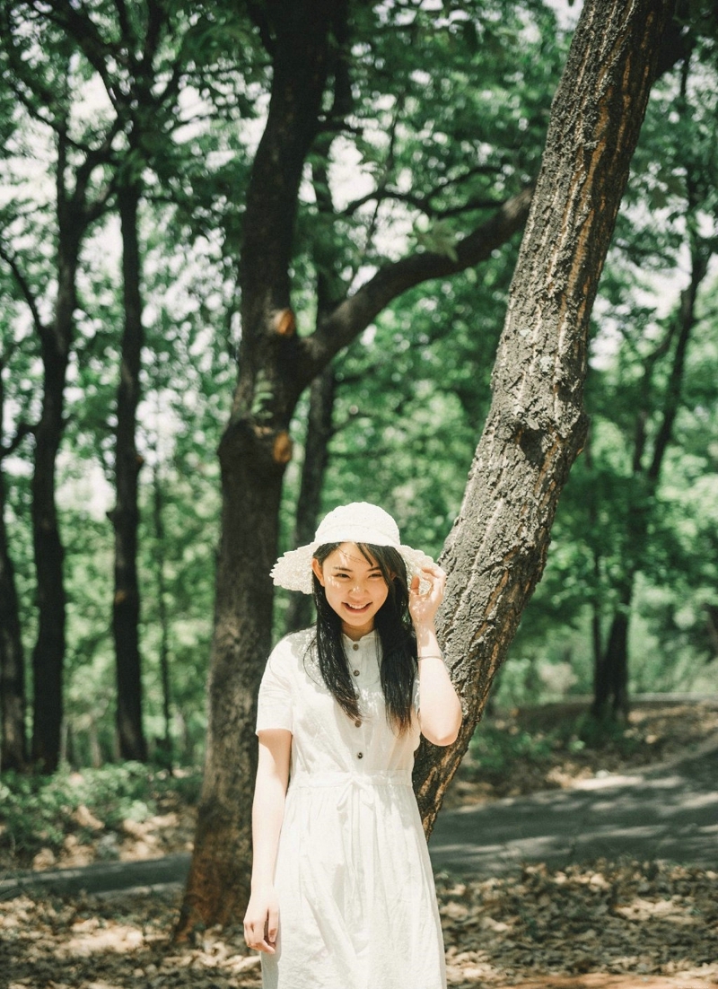 森林公园内的白裙草帽背包少女清爽怡人